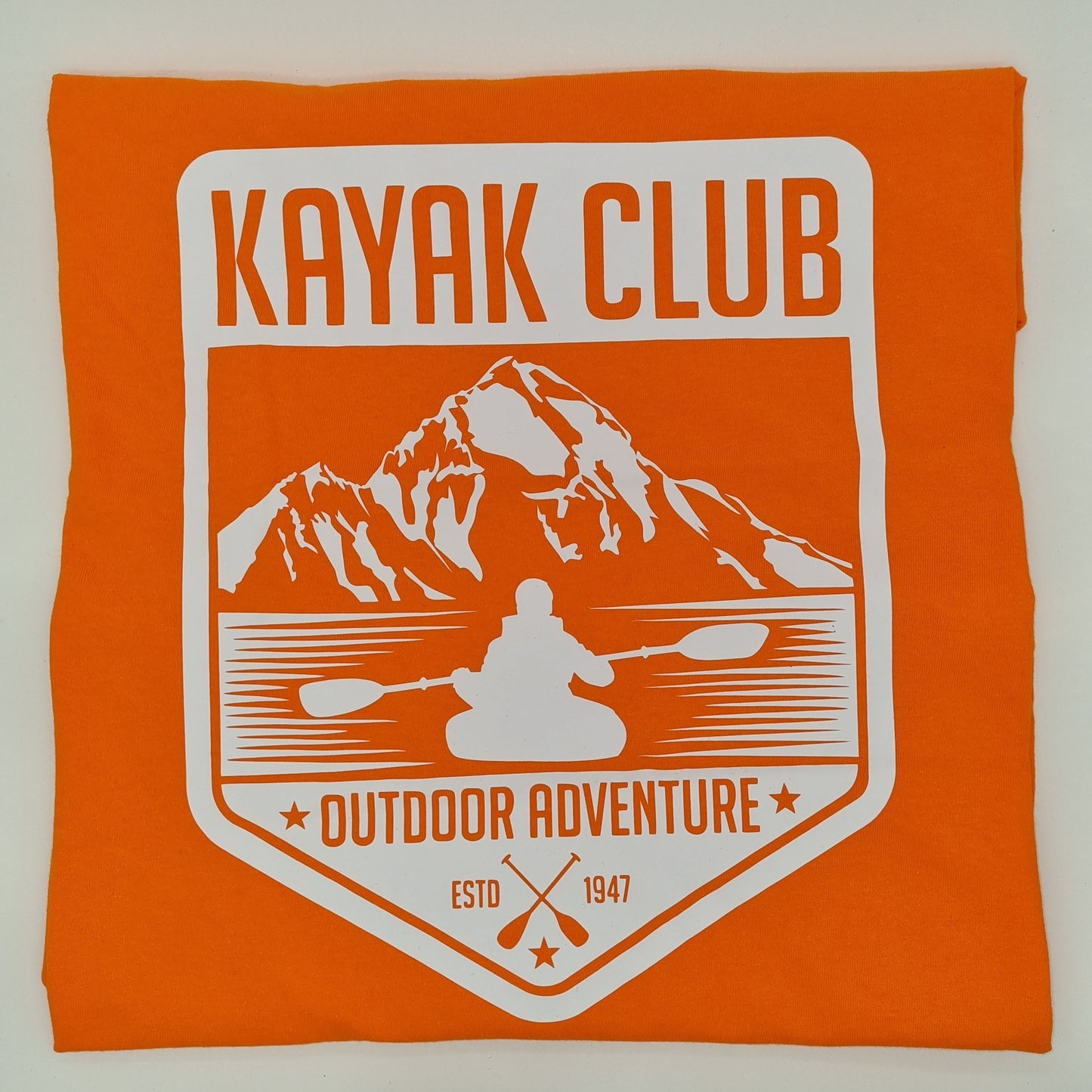 Orange t-shirt with a white graphic of someone kayaking in front of a mountain